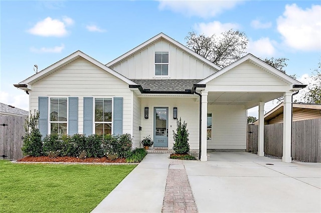 view of front of property with fence, a shingled roof, a front lawn, concrete driveway, and board and batten siding