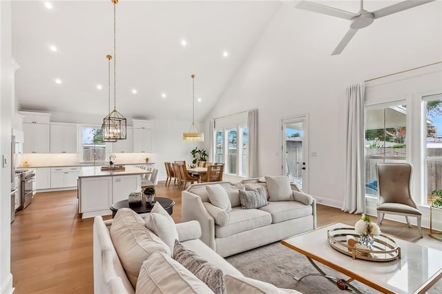 living room featuring baseboards, light wood finished floors, high vaulted ceiling, recessed lighting, and ceiling fan with notable chandelier