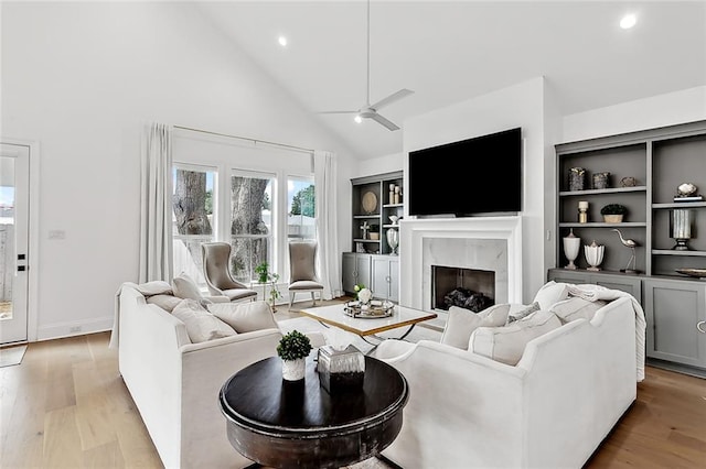 living room with a high end fireplace, light wood-style flooring, high vaulted ceiling, and a ceiling fan