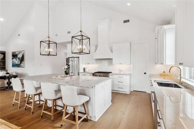 kitchen with visible vents, a kitchen island, custom exhaust hood, stainless steel fridge, and a sink