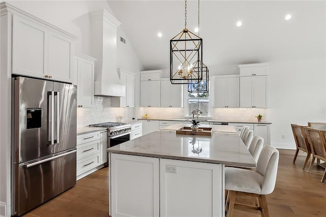 kitchen with a kitchen island, a breakfast bar, white cabinetry, high end appliances, and hanging light fixtures