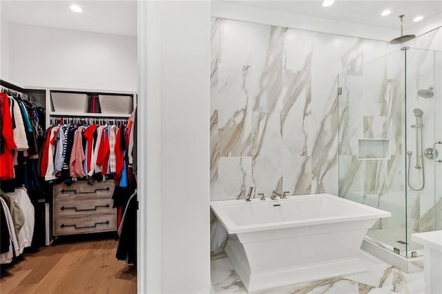 bathroom with a walk in closet, marble finish floor, recessed lighting, a marble finish shower, and a freestanding bath