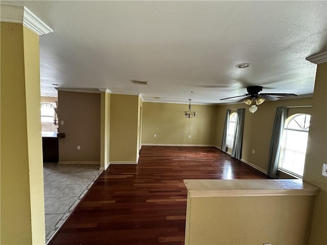 unfurnished room featuring crown molding, a healthy amount of sunlight, dark wood-type flooring, and ceiling fan with notable chandelier