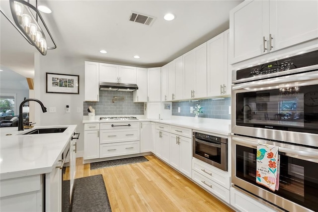 kitchen featuring sink, white cabinets, double oven, and tasteful backsplash