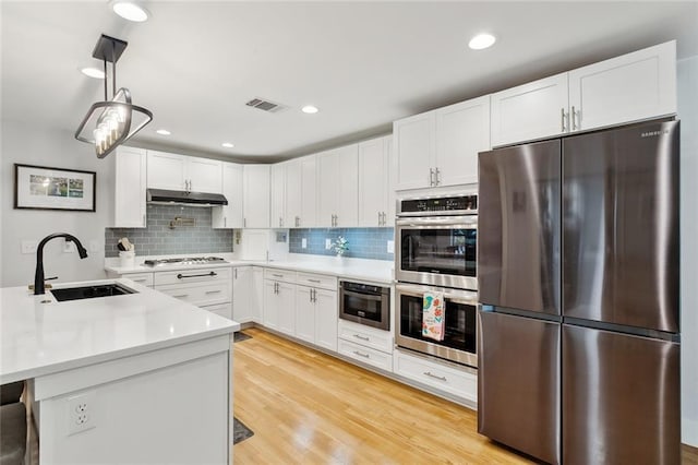 kitchen with stainless steel appliances, white cabinets, pendant lighting, light hardwood / wood-style flooring, and sink