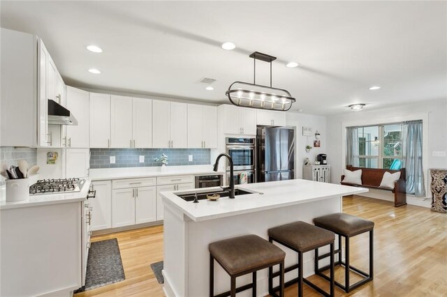 kitchen with stainless steel appliances, white cabinets, decorative light fixtures, and a kitchen island with sink