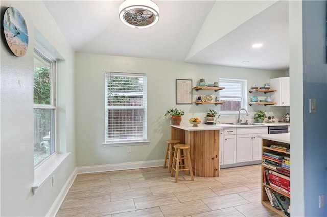 kitchen with a healthy amount of sunlight, lofted ceiling, white cabinets, and sink