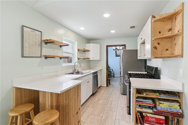 kitchen with kitchen peninsula, a kitchen bar, sink, white cabinetry, and appliances with stainless steel finishes