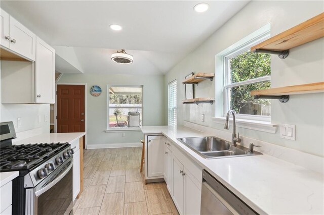 kitchen with appliances with stainless steel finishes, white cabinetry, sink, kitchen peninsula, and vaulted ceiling