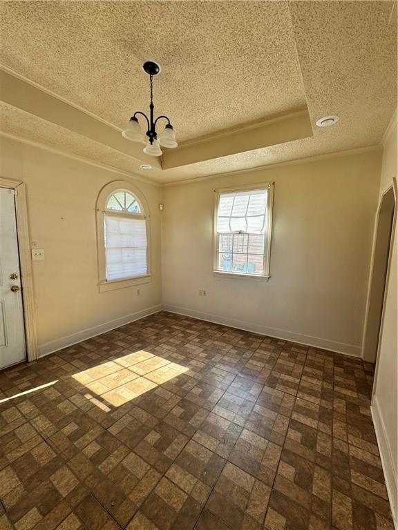 empty room with crown molding, a raised ceiling, and a notable chandelier