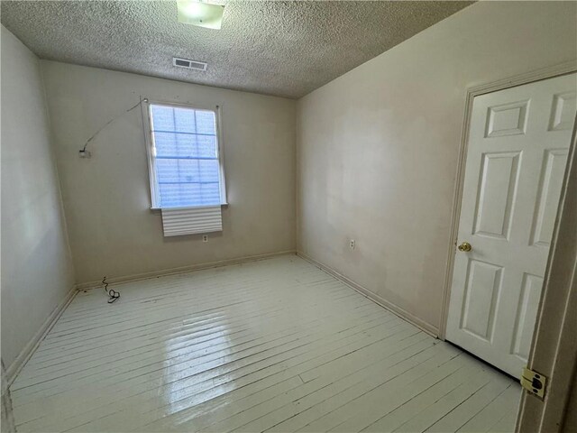 spare room with light wood-type flooring and a textured ceiling