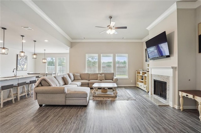 living room with dark wood-type flooring, a fireplace, sink, ceiling fan, and crown molding