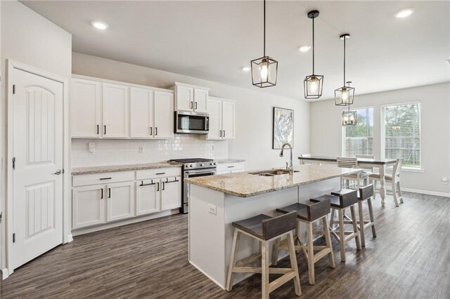 kitchen with an island with sink, appliances with stainless steel finishes, pendant lighting, white cabinets, and sink