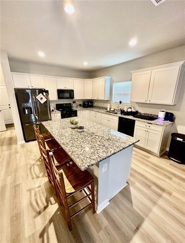 kitchen with a breakfast bar area, white cabinetry, light stone counters, black appliances, and a kitchen island