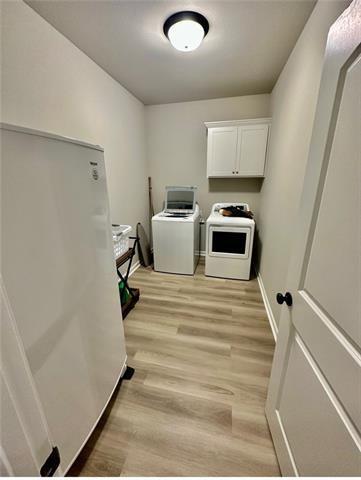 clothes washing area featuring washer and clothes dryer, cabinets, and light wood-type flooring