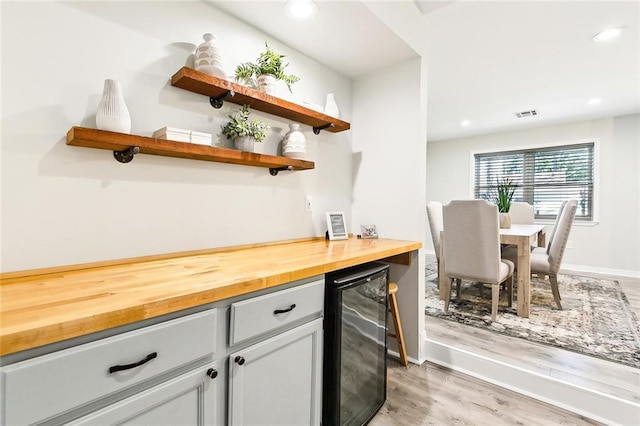 bar featuring butcher block countertops, light wood-type flooring, beverage cooler, and gray cabinets