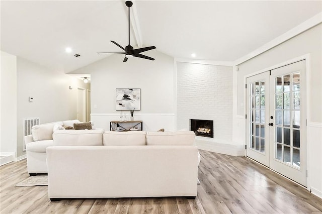 living room featuring ceiling fan, light wood-type flooring, lofted ceiling, a fireplace, and french doors