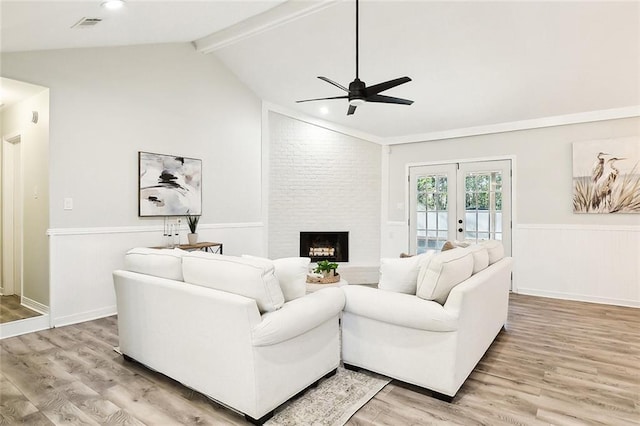 living room with french doors, a fireplace, vaulted ceiling with beams, ceiling fan, and light hardwood / wood-style flooring