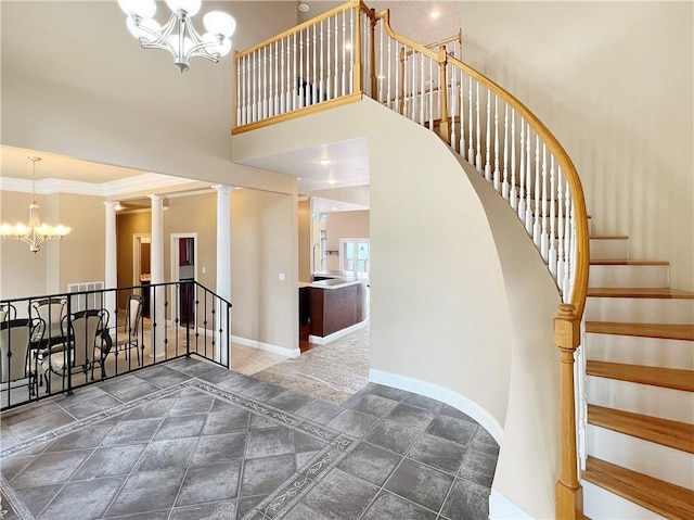 stairway featuring a towering ceiling, ornamental molding, a chandelier, and ornate columns