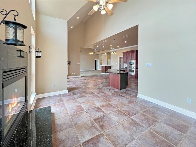 kitchen with ceiling fan, a kitchen bar, high vaulted ceiling, stainless steel microwave, and a center island with sink