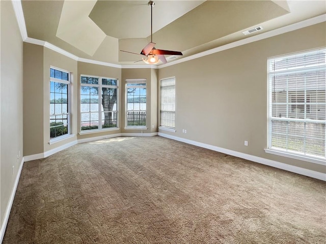 empty room with vaulted ceiling, carpet floors, ornamental molding, ceiling fan, and a tray ceiling