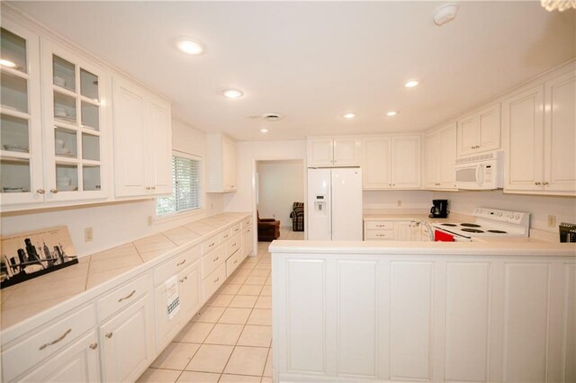 kitchen featuring white cabinets, kitchen peninsula, light tile patterned flooring, and white appliances