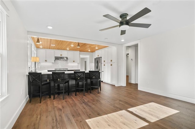 kitchen featuring kitchen peninsula, ceiling fan, backsplash, a kitchen breakfast bar, and white cabinets