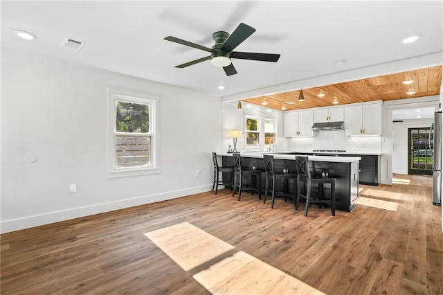 kitchen with ceiling fan, kitchen peninsula, white cabinetry, light wood-type flooring, and a breakfast bar area