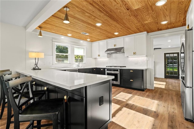 kitchen featuring white cabinetry, a kitchen bar, kitchen peninsula, appliances with stainless steel finishes, and light hardwood / wood-style flooring