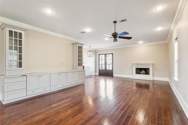 unfurnished living room with ceiling fan, dark wood-type flooring, and ornamental molding