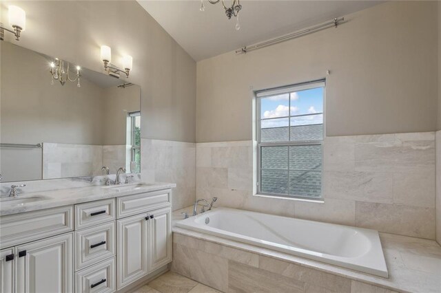 bathroom featuring lofted ceiling, tile patterned floors, vanity, tile walls, and tiled bath