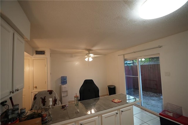 kitchen with ceiling fan, tile countertops, light tile patterned floors, a textured ceiling, and white cabinets