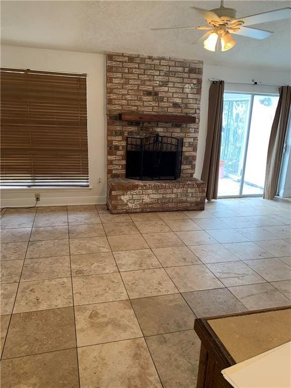 unfurnished living room with ceiling fan, a textured ceiling, light tile patterned floors, and a brick fireplace