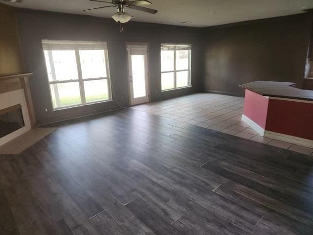 unfurnished living room featuring ceiling fan, dark wood-type flooring, and a wealth of natural light