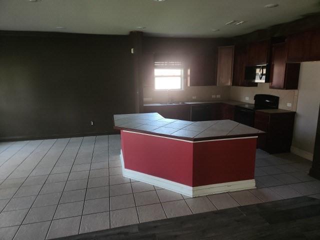 kitchen featuring light tile patterned floors, tile countertops, a kitchen island, and black appliances