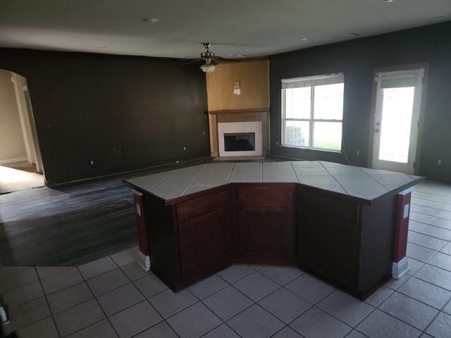 kitchen with ceiling fan, kitchen peninsula, tile countertops, and light tile patterned flooring