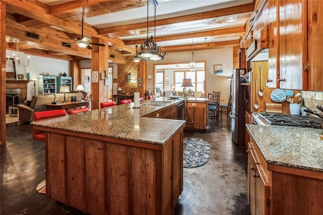 kitchen featuring sink, decorative light fixtures, a kitchen island with sink, stone countertops, and beamed ceiling