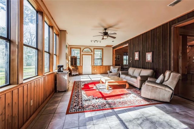 tiled living room with ceiling fan and wood walls