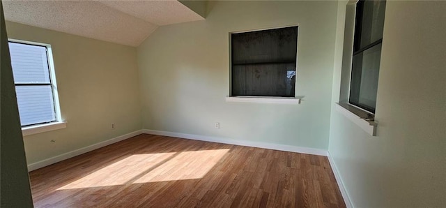 unfurnished room with a textured ceiling, lofted ceiling, and wood-type flooring