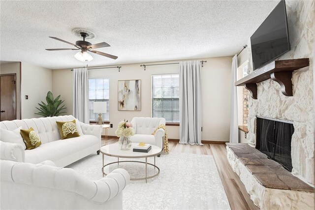 living room featuring ceiling fan, a textured ceiling, light hardwood / wood-style flooring, and a fireplace