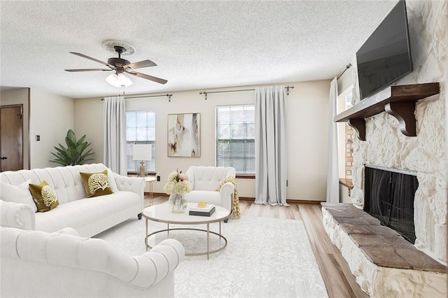 living room featuring ceiling fan, light wood-type flooring, a stone fireplace, and a textured ceiling