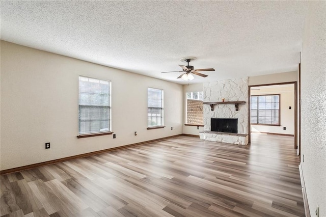 unfurnished living room with ceiling fan, light wood-type flooring, a fireplace, and a textured ceiling