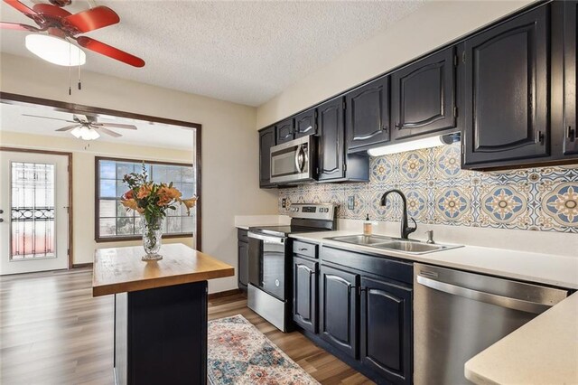 kitchen with appliances with stainless steel finishes, tasteful backsplash, a textured ceiling, light hardwood / wood-style flooring, and sink