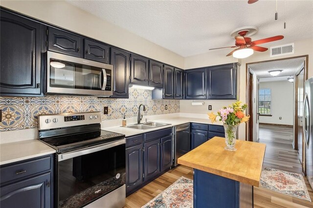 kitchen with appliances with stainless steel finishes, sink, butcher block countertops, light hardwood / wood-style flooring, and blue cabinets