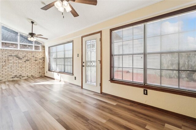 unfurnished living room with ceiling fan, brick wall, light hardwood / wood-style flooring, and lofted ceiling