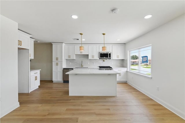 kitchen featuring appliances with stainless steel finishes, a center island, hanging light fixtures, white cabinets, and sink