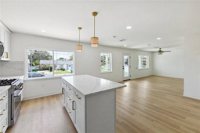 kitchen featuring stainless steel range, ceiling fan, hanging light fixtures, a kitchen island, and light stone counters