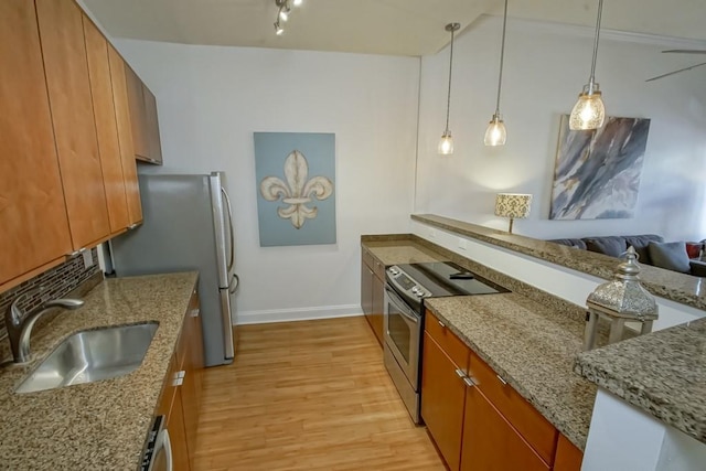 kitchen featuring stainless steel appliances, pendant lighting, light hardwood / wood-style flooring, light stone counters, and sink