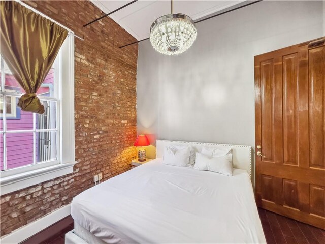 bedroom featuring dark wood-type flooring, brick wall, and a chandelier