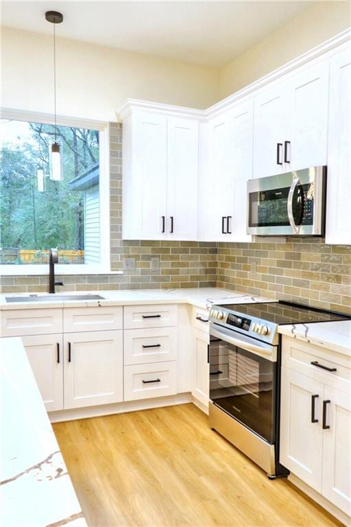 kitchen featuring white cabinets, stainless steel appliances, decorative backsplash, light hardwood / wood-style floors, and hanging light fixtures